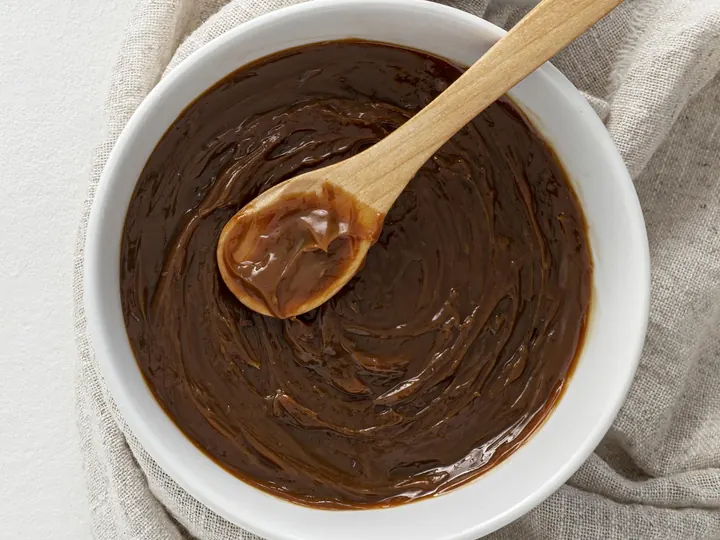 Dulce de leche casero espeso en un bol, con una cuchara de madera